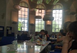 Arbeitsgruppe in der Hochschule München FB 11 Pasing, Leute mit Gläsern und Tassen um einen Tisch, im Hintergrund hohe Fenster